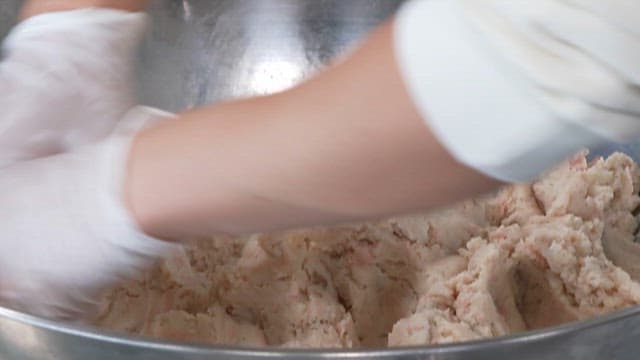 Hands Mixing Mashed Potatoes and Ham in a Metal Bowl