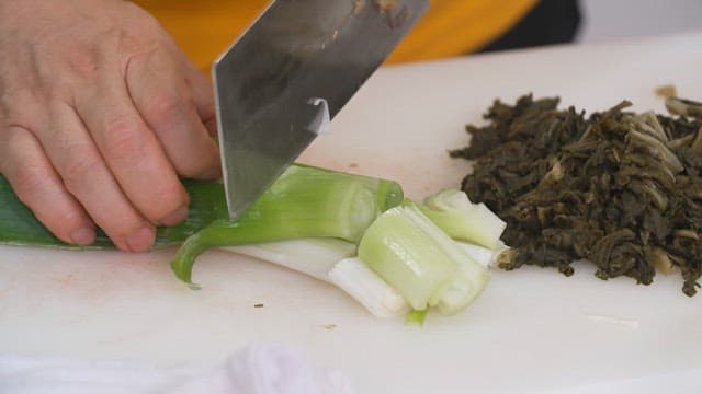 Cutting fresh green onions with a knife on a cutting board