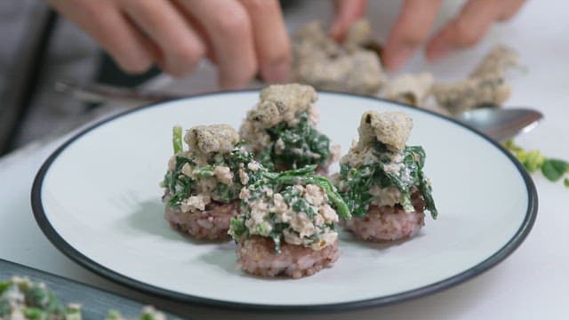 Hands garnishing a dish with leafy vegetables and toppings