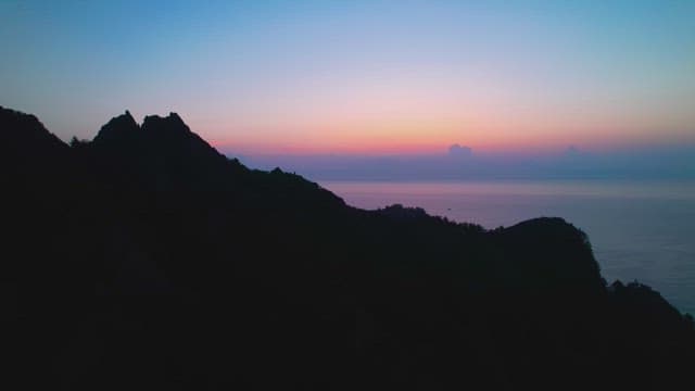 Sunset over the ocean with shadowed mountains