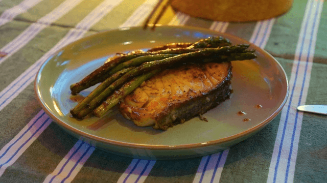 Fish steak and asparagus neatly placed on a plate on a cozy table