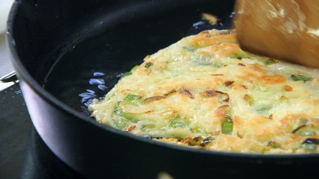 Crispy green onion pancakes sizzling in a frying pan