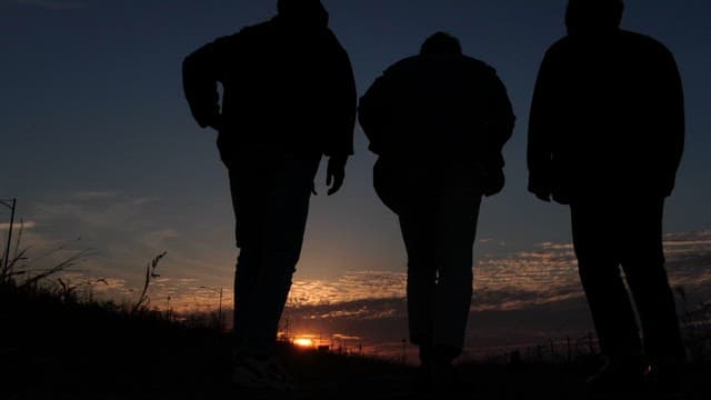 Three people walking in the dark sky at sunset