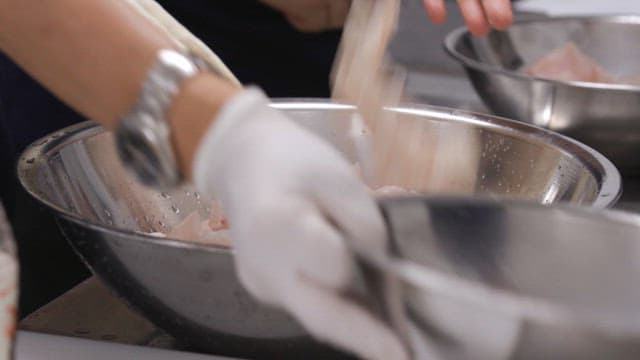 Chef seasoning sashimi in a stainless steel bowl in the kitchen