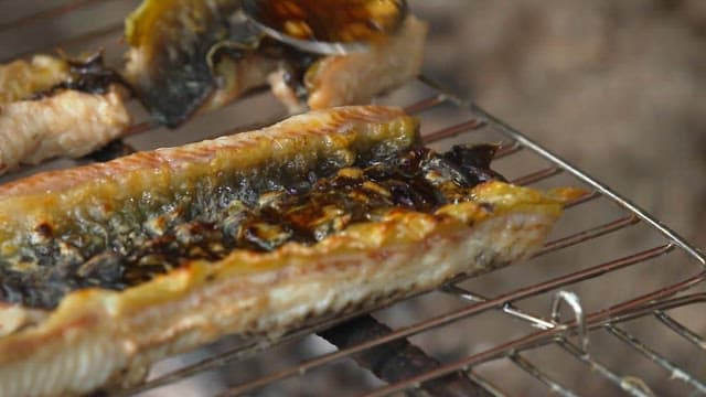 Applying sauce to eel grilled over charcoal