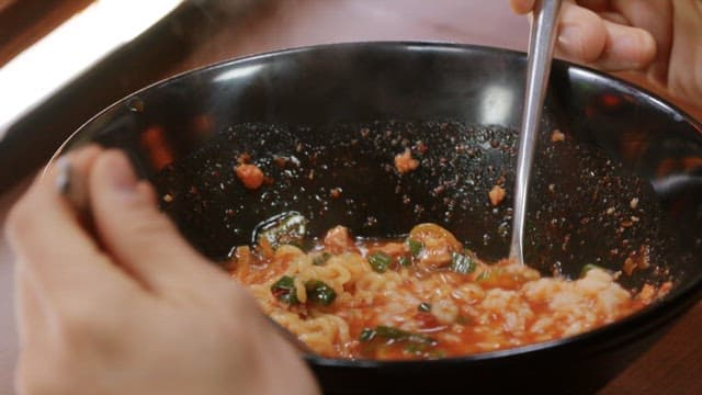 Black bowl of spicy ramen with rice in it