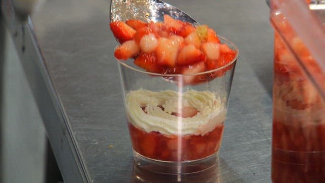 Preparing dessert by placing strawberry slices in a glass with cream