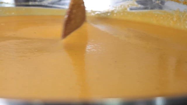 Yellow soup being stirred in a pot