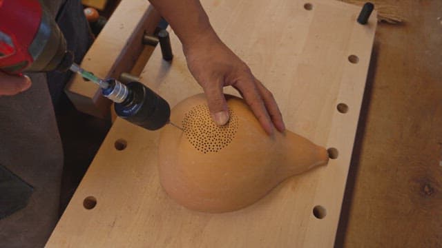 Person drilling a gourd on a workbench