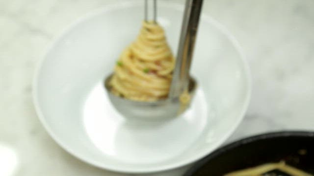 Plating spaghetti in a white bowl with chopsticks and ladle