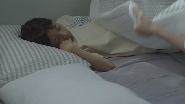 Mother tucking in her sleeping daughter in a dimly lit room