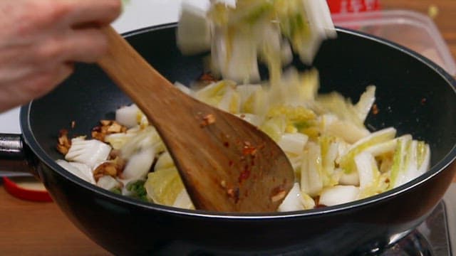 Stirring fresh cabbage in a frying pan on a stove