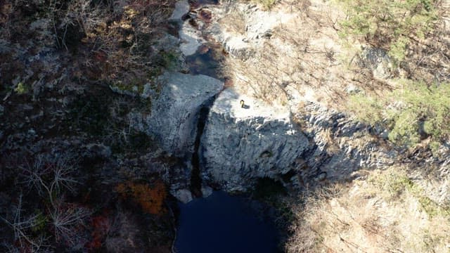 Daytime scene with people standing near a cliff and mountains in the background