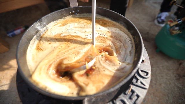 Broth in the pot is stirred with a ladle