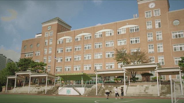 Kids playing soccer in front of a large school building