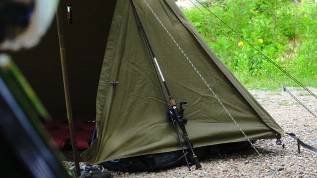 Tent pitched on a gravel ground with fishing rods resting against it
