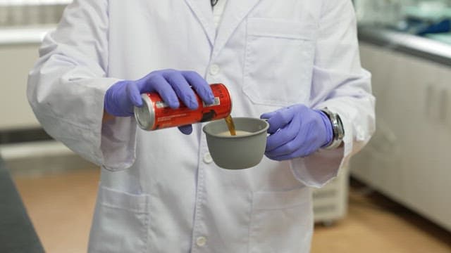 Scientist pouring canned cola into a gray cup for an experiment