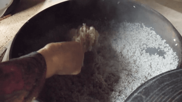 Scooping freshly cooked barley rice from a steaming cauldron