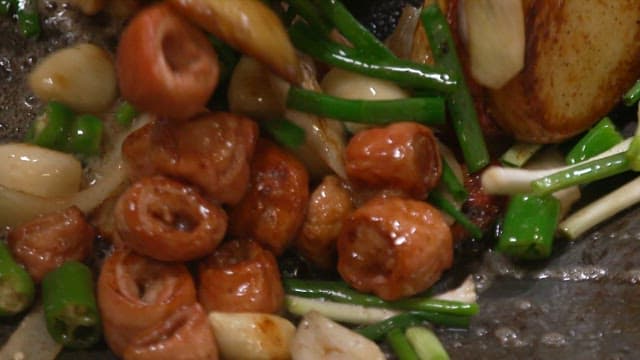 Grilled pork intestines being cooked in a frying pan with garlic and green onions