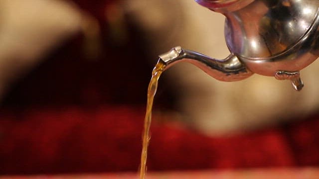 Mint tea being poured into a glass on a patterned table