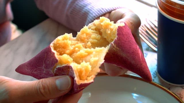 Hands breaking open a steamed purple sweet potato indoors