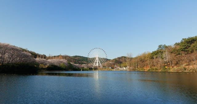 A serene lakeside view with a Ferris wheel in the background on a clear day