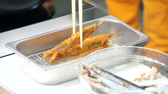 Plating the golden and crispy skewered sand eels on a metal plate with chopsticks