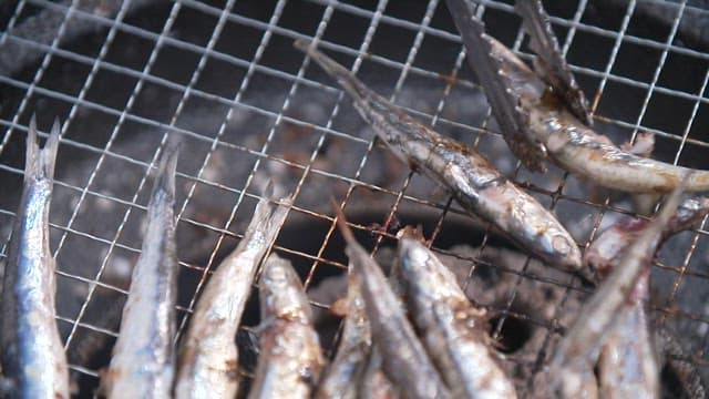 Grilling anchovies on a grill using tongs