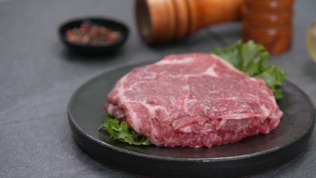 Raw steak on a black plate with seasoning