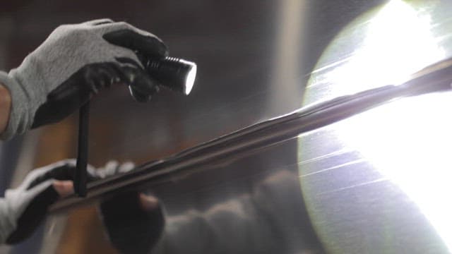 Gloved hand inspecting a metal surface with a flashlight