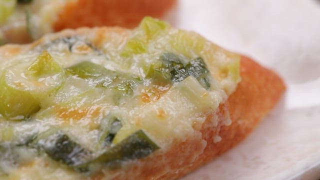 Crispy and appetizing baguette topped with green onions and cheese on a plate