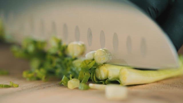 Knife Slicing Green Onions on a Cutting Board