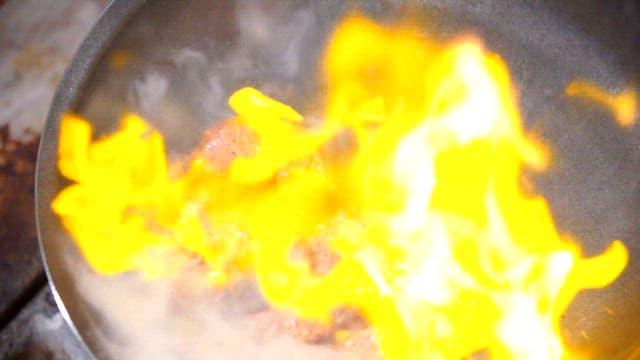 Flames rising from a pan with beef cooking