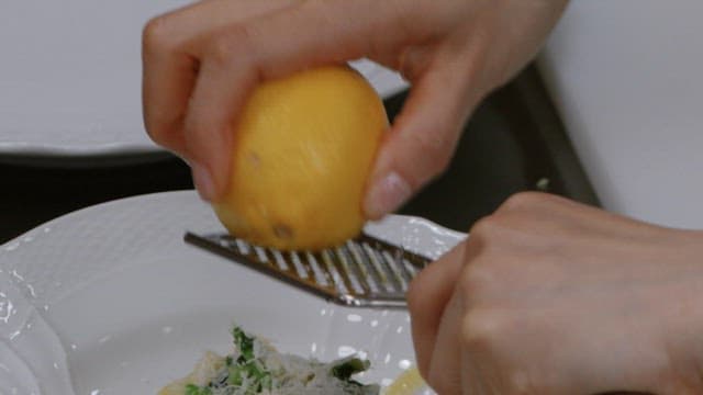Sprinkling lemon zest over the pasta dish.