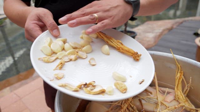 Preparing Samgyetang with fresh chicken, ginseng, and garlic in a pot