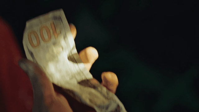 Hands Crumpling 100 Dollar Bills in the Dark