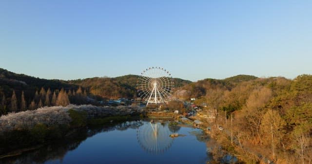 Large Ferris wheel surrounded by lush forest and a reflective lake