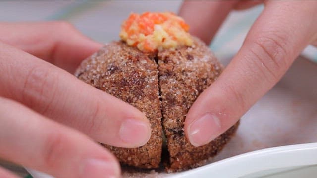 Hands splitting a glutinous rice donut made of carrot