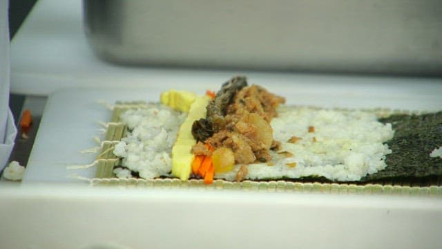 Plastic gloved hands preparing kimbap with mustard leaves