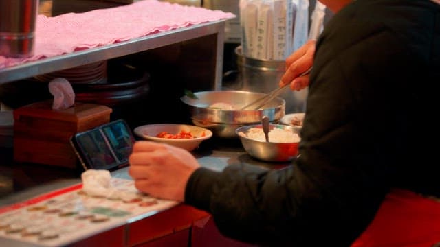 Person eating ginseng chicken soup while watching a video on a smartphone
