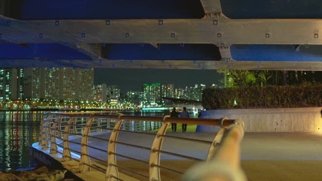 People walking on the city's riverside promenade under the bridge at night
