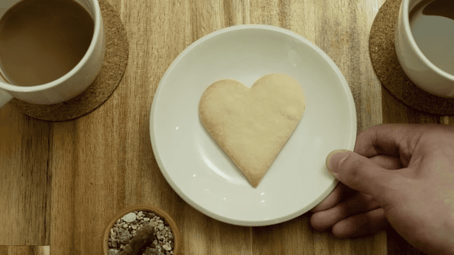 Two cups of coffee with a heart-shaped cookie on wooden table