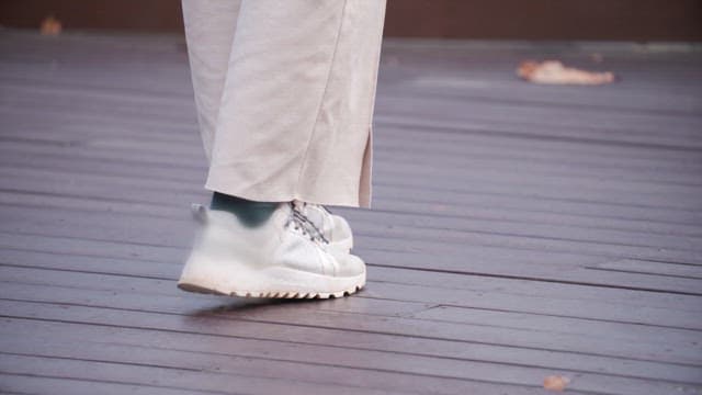 Feet of person walking on wooden deck wearing sneakers