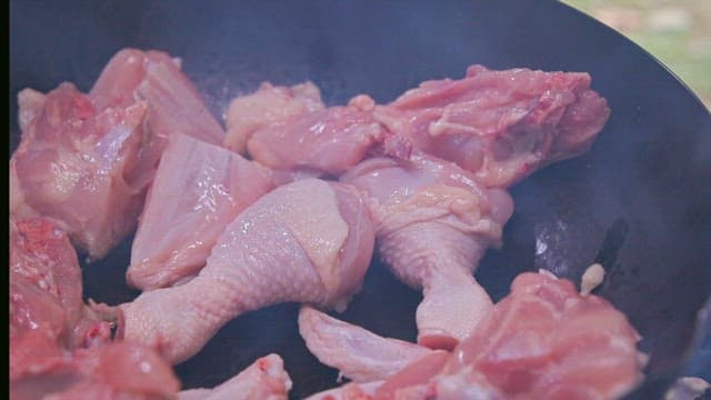 Raw chicken pieces cooked in a frying pan