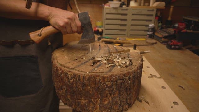Person carving wood with an axe indoors