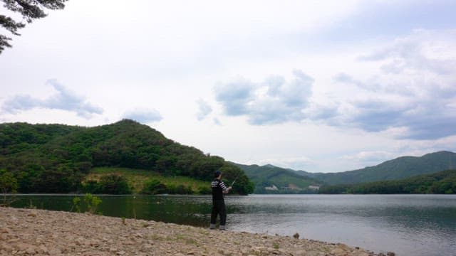 Person fishing by the serene lake on a cloudy day
