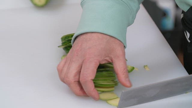Cutting zucchini into strips with a knife on a cutting board