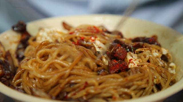 Mixing noodles in thick black bean sauce sprinkled with red pepper powder with chopsticks