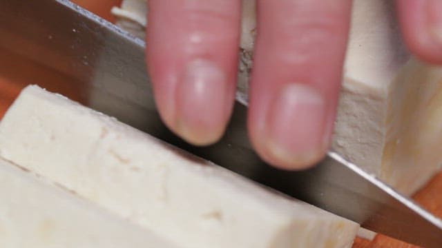 Fresh tofu cut with a knife on a cutting board