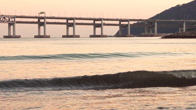 Waves Crashing Ashore Near a Large Bridge